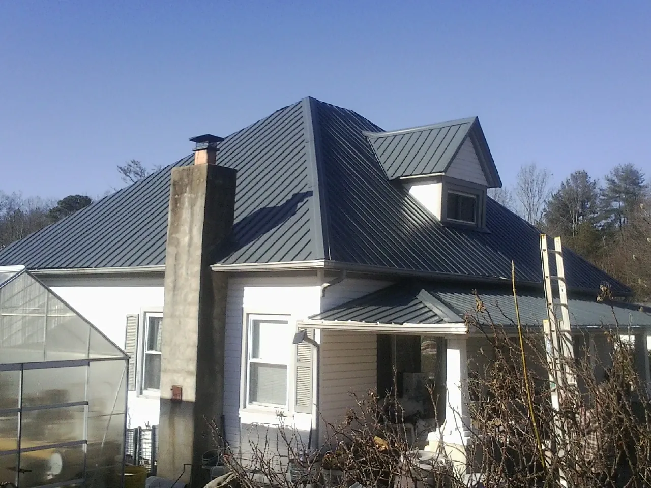 Dark blue standing seam metal roof on a white farmhouse with dormer — Slate & Tile Roof Repair by Roofing Brothers in Northfield